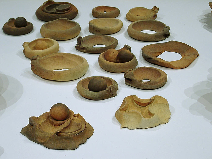 an array of low round clay fired bowls some with balls of clay embedded and some with tracks or marks where balls of clay once landed or moved, a detail from cazuelas, beginnings, an installation by gabriel orozco at documenta 11 in 2002.