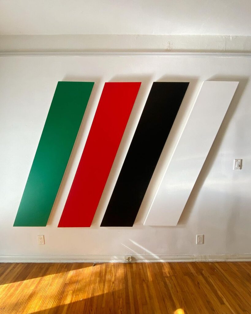 joshua smith 1983 just posted this image to his instagram of four elongated parallelogram shaped monochrome paintings leaning to the right, in the colors green, red, black, and white, hung on a white wall with a similarly proportioned parallelogram of sunlight hitting the hardwood floor below. a work titled Untitled (Forbidden Colors), 2024, after a related work from 1988 by Felix Gonzalez-Torres, which is in the collection of MOCA LA.