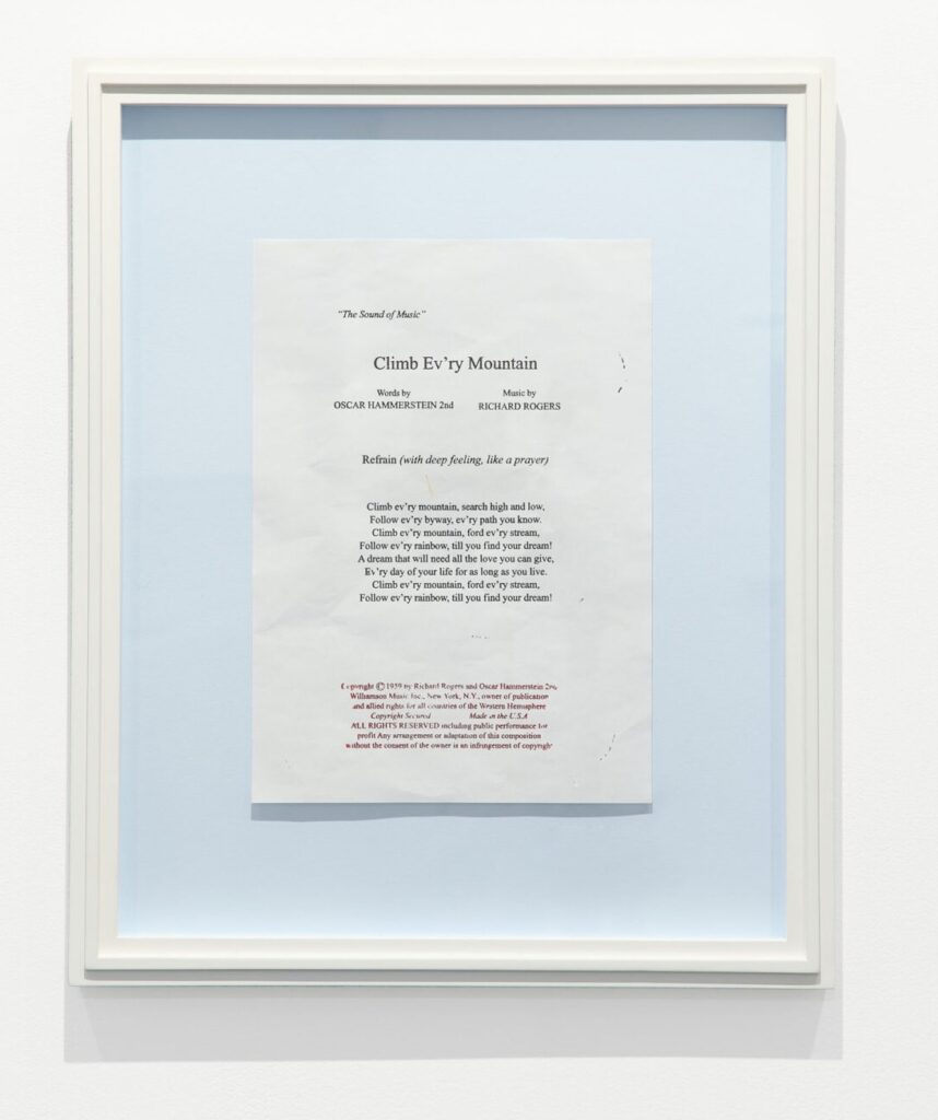 robert gober print of the lyrics to rogers & hammerstein's climb ev'ry mountain from the sound of music on white paper mounted on a light blue board in a white painted wood frame, from an edition of 15 on view at krakow witkin gallery. the text is printed in black, and the copyright notice at the bottom in red, using engraved potatoes.