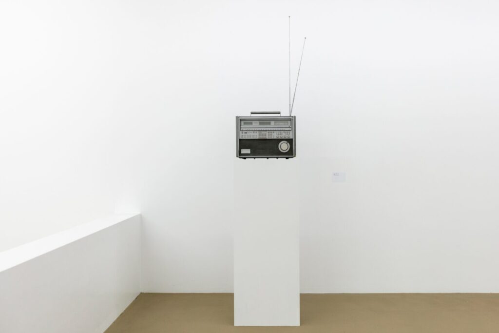 isa genzken sculpture, weltampfanger, 1982, is a readymade, a panasonic rf-9000 shortwave radio in black and silver, with dials and buttons and two antennas, on a white pedestal of the same width, installed on a mezzanine in the white cube style gallery of the kunstmuseum basel in 2020. photo julian salinas