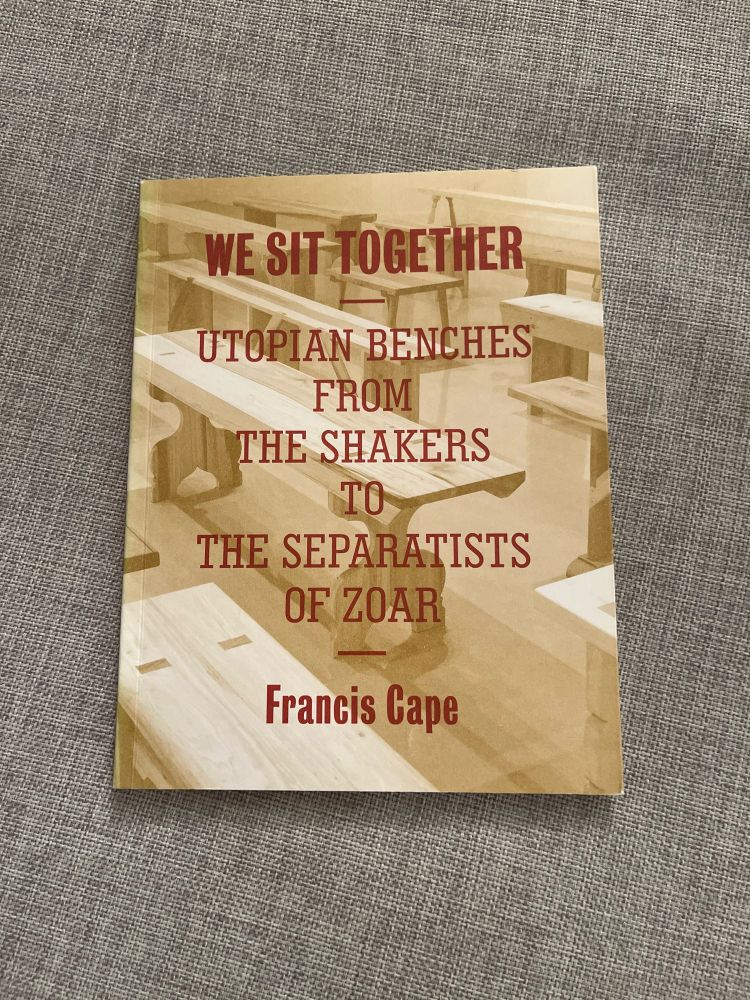 the cover of francis cape's 2013 exhibition catalogue, we sit together: utopian benches from the shakers to the separatists of zoar, has the title printed in red over a duotone photo of the benches installed in rows. the book sits on a linen background in this photo by andrew russeth