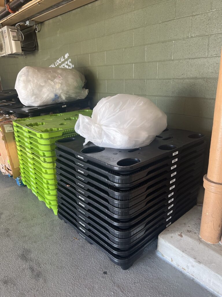 in a whole foods parking garage a stack of black plastic nestable pallets sits next to a stack of chartreuse nestable pallets of a different model, but same concept, while garbage bags of paper rest atop them. the black pallets are identical to the ones cady noland includes in her installation at glenstone, though so far, she has not identified them as a work or part of a work, just part of the landscape, like here.