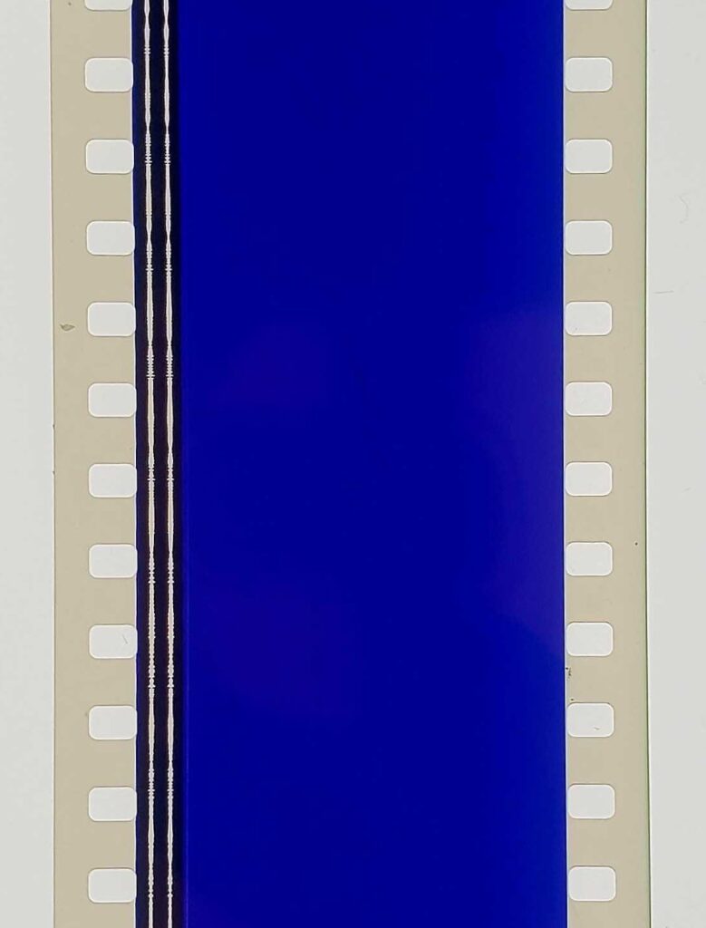 a vertical strip of 35 millimeter film stock is entirely blue, with two white waveforms of an optical audio track running in black down the left side. sprocket holes punctuate either side of the film strip. this is apparently a piece of a print of derek jarman's monochrome blue film, Blue, made in 1993, as he was losing his sight as a side effect of aids and related medications.