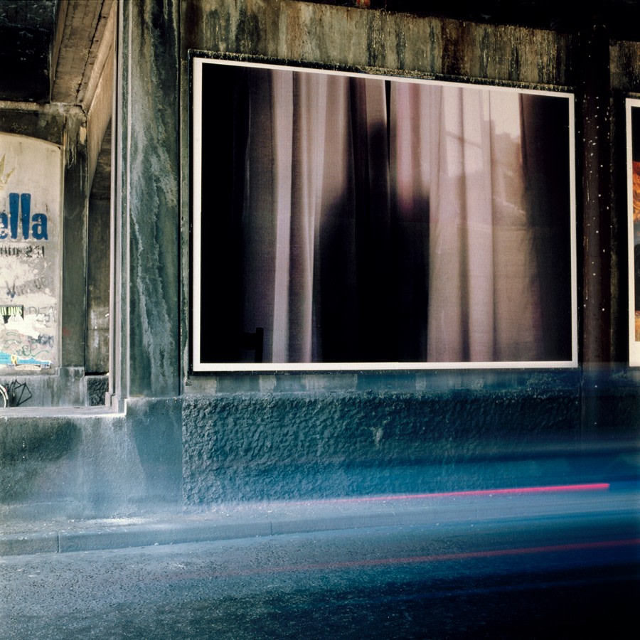 a billboard by felix gonzalez torres of a dark snapshot of the silhouette of a figure behind a sheer curtain was installed on a rough congrete wall along a street in copenhagen in 1992