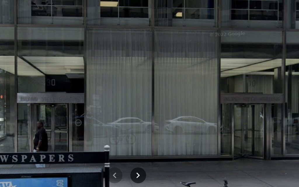 google streetview image of the steel and glass lobby of chicago's inland steel building with two white curtains hanging inside, between the two revolving doors. circa 2022