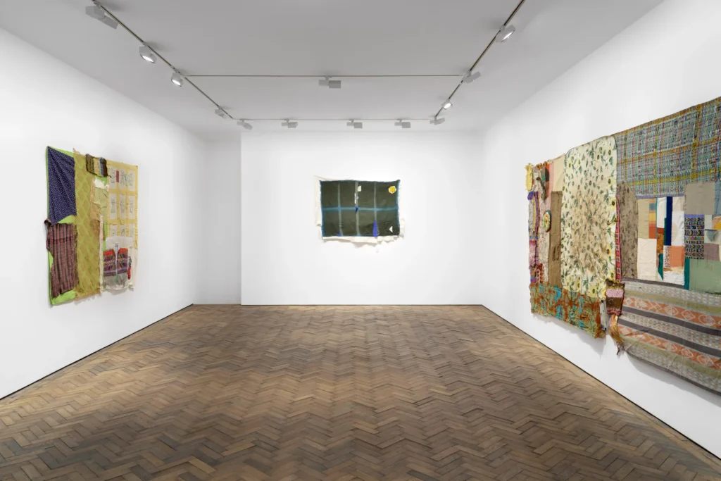 three textile works by susan cianciolo hang, one on each of three walls in a white walled gallery with a herringbone brick floor at stuart shave modern art in london.