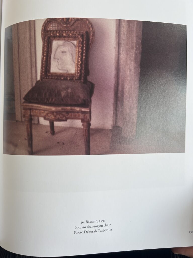 a page from homes & studios with a large blurry 1991 photo by deborah turbeville, printed beyond its resolution capacity for aesthetic effect. it depicts what is called in the caption a picasso drawing on a chair. the drawing of the head of a woman in profile is in an extremely ornate carved frame, and the chair is also ornately carved with a dark upholstered velvet seat. it sits between two stone doorframes on a marble floor, in the palazzo cy twombly bought in bassano, italy. except it turns out that twombly made this copy of a picasso drawing, nicola del roscio probably knew that when he put this caption in the book in 2019, but it's not clear whether turbeville knew it when she made the photo.