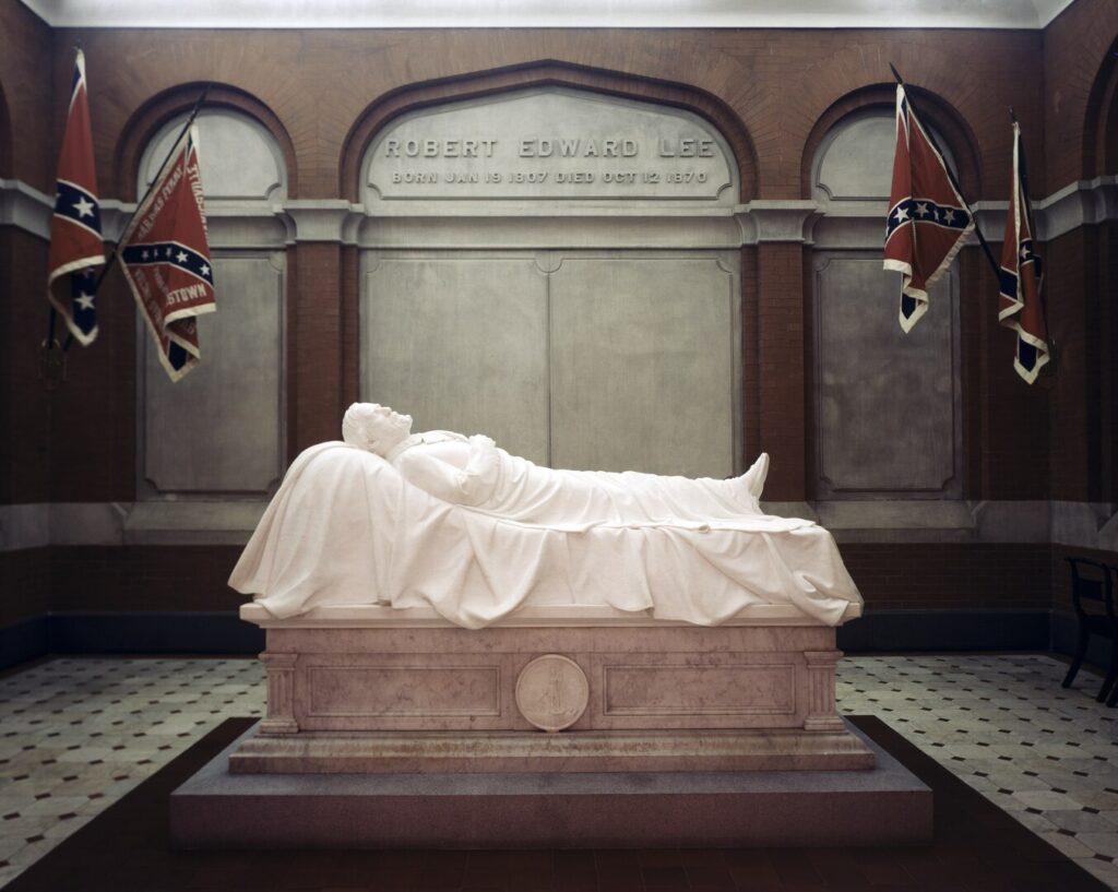 a white marble statue of robert e lee lounging, on a pedestal where a normal church would have its altar, with his name in raised marble letters in the center of three arched nooks in the brick and marble wall behind. four confederate flags of a specific type of great interest to people who really really care about such things as white supremacism and dismissing slavery and whatever, idgaf. the floor is white marble with little black corner tiles, a pattern which was adopted by shitty linoleum makers and propagated to the kitchens of rentals across the north east, where it lay in wait to be discovered and ripped out decades later. washington & lee university changed the name of this building to university chapel, which is like putting another layer of shitty linoleum down over the old one. anyway, the sculpture's by racist edward valentine