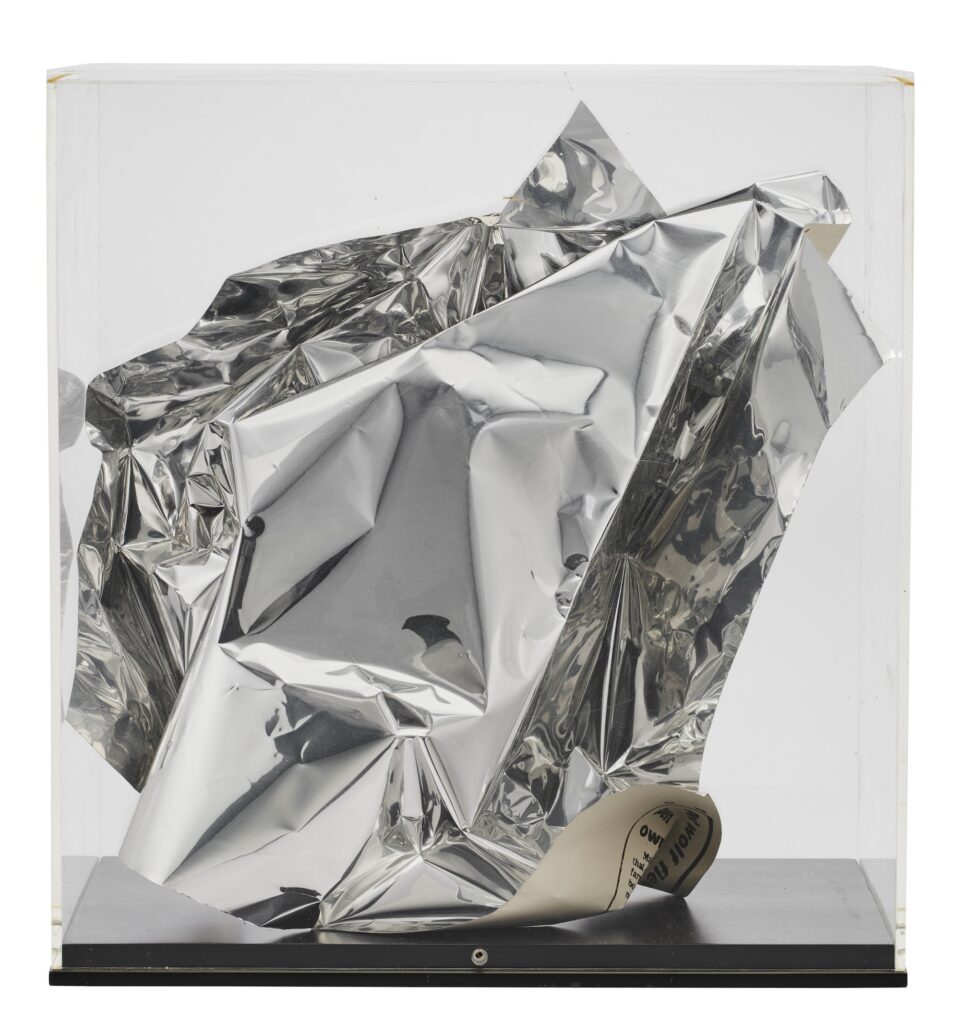 the back of the warhol screenprinted newspaper page sculpture shows the mirror finish surface of the aluminum sheet, crumpled into an abstract sculpture, in that vitrine obv. via christie's