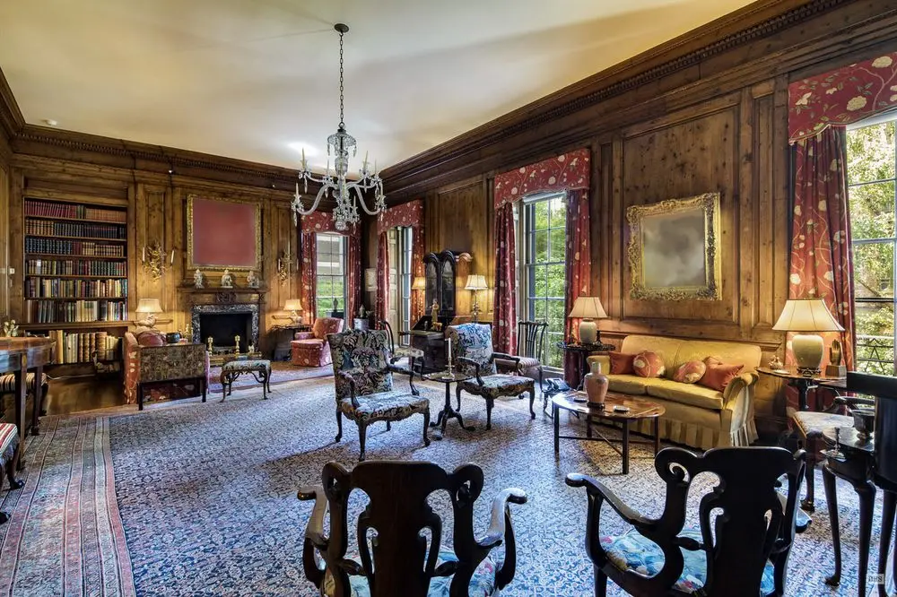 a 2018 real estate listing photo of the 2nd floor living room of david and peggy rockefellers' extremely wide east 65th st townhouse shows wood paneled walls, a giant persian carpet, several seating areas with antique chairs and upholstered sofas, a lot of table lamps, tall casement windows, a built in bookcase in one corner, a thin chandelier in the center of the unadorned ceiling, which is nonetheless surrounded by a thick af carved wood crown moulding, but the point here is, the painting over the fireplace at the far end of the room is blurred out with a terra cotta square, and the painting between the windows on the north wall, over a yellow sofa, is blurred out, too. both these pictures were for sale at the same time as the house though, so wtf? the first is a bonnard, the second a corot.