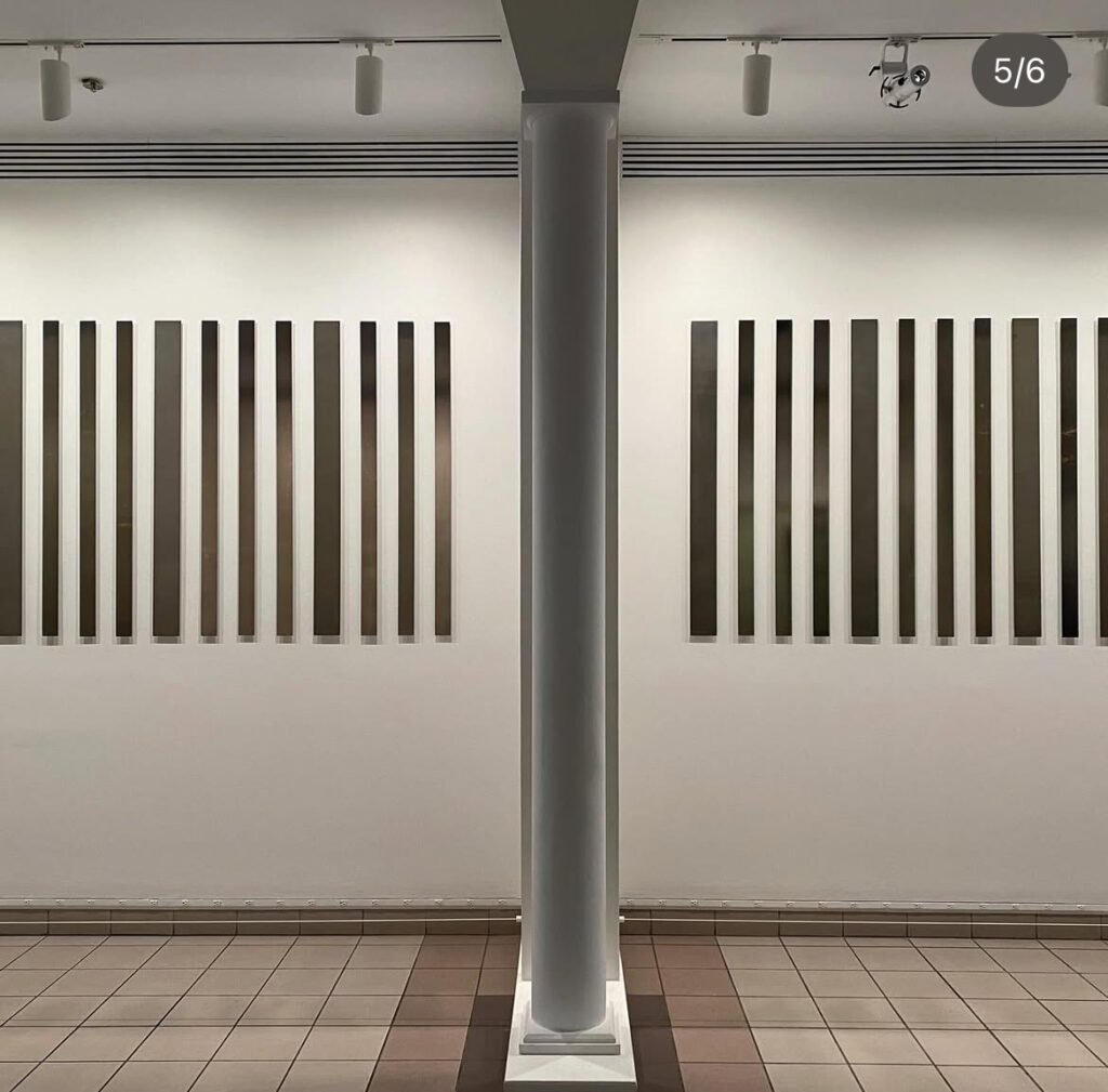 long, narrow, vertical strip photograms of varying shades of silver and of varying widths are installed on the wall on either side of a column at the george eastman museum, a show of liz deschenes' work in 2025