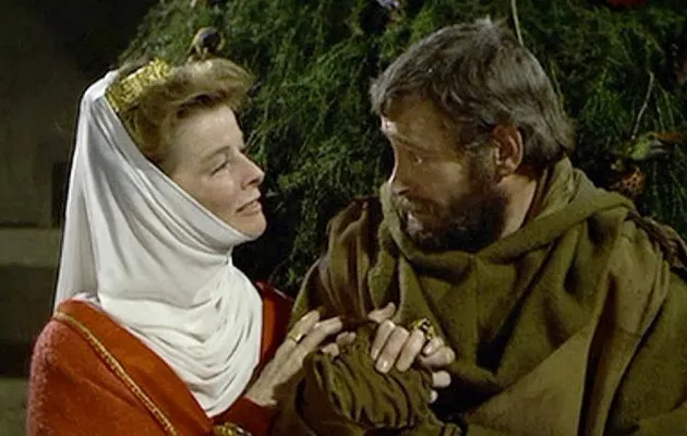 a still from anthony harvey's 1968 film, a lion in winter, in which katharine hepburn, a scarf wrapped tightly under her chin and attached to the bun coming through the top of her small gold crown, looks intensely, while holding his arm, into the eyes of peter o'tool, who is here in a thick brown monk's habit, full beard, and no head gear.