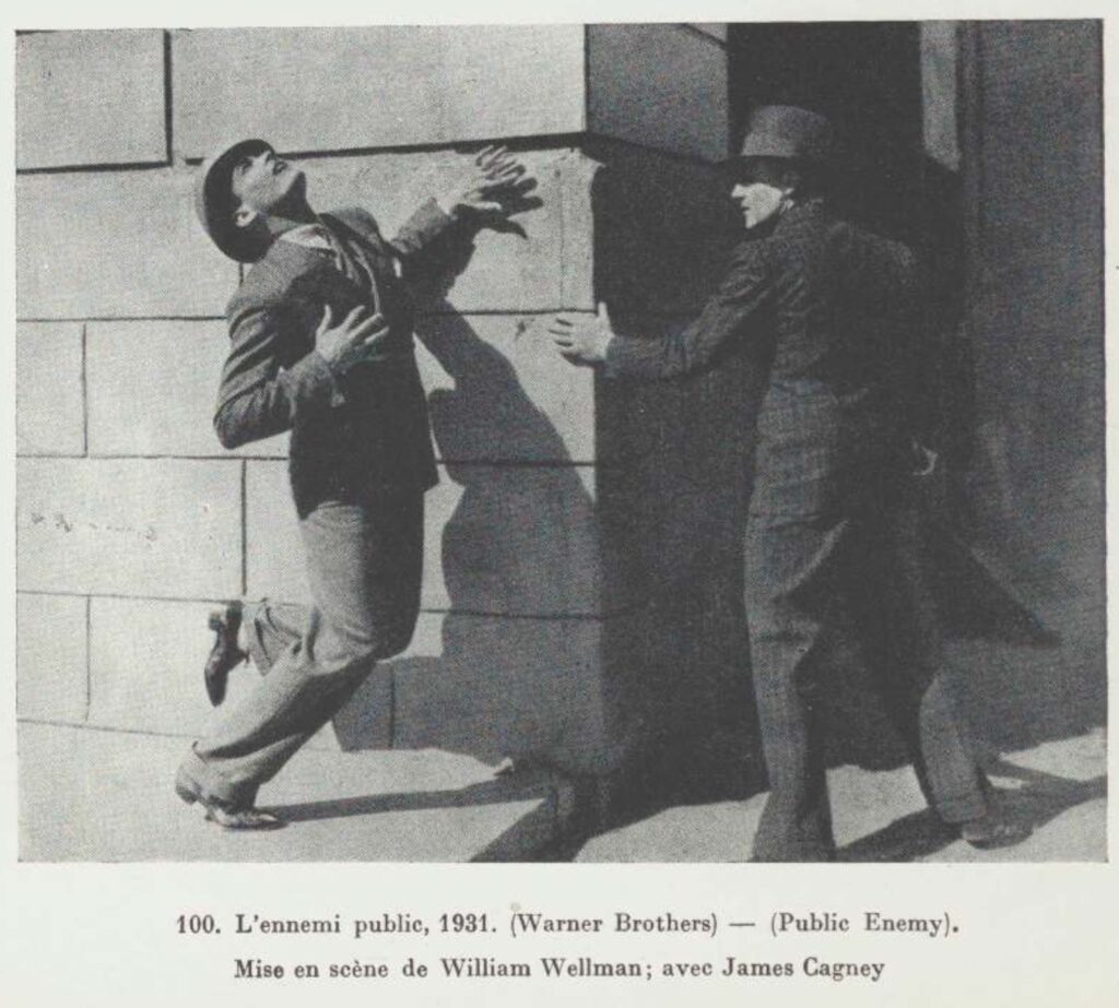 a black and white still from the 1931 warner brothers film, the public enemy in which two white men in suits and hats are facing each other at the corner of a heavy stone building. the one on the left, in the bright daylight, is beginning to fall from being shot in the back. the one on the right, james cagney, btw, in the shadowy side more protected from the ambush, is holding the edge of the building. the picture is reproduced in a moma catalogue published in france in 1938, and has a caption, "100 l'ennemi public, 1931. warner brothers (public enemy). Mise en scene de william wellman; avec james cagney," like i was saying. via moma.org