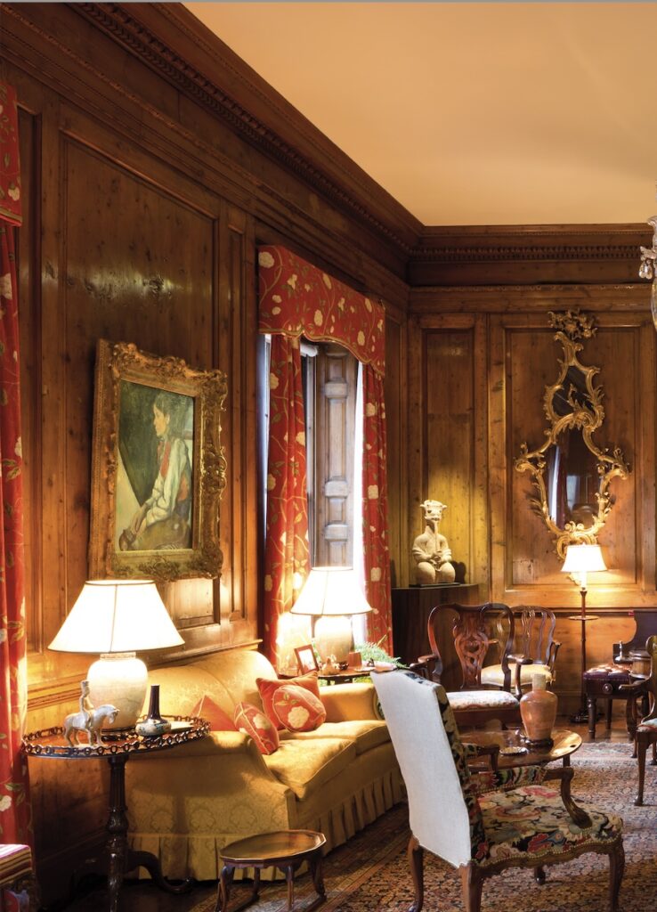 a pic of the rockefeller's 65th st living room with cezanne's boy in a red vest, a 1955 gift to moma, with some strings, hanging between two red curtained tall windows and over a yellow sofa. table lamps on various chippendale pie crust tables give the whole wood palneled room a golden glow. there is an ancient figure of a seated pipe player of some kind in the corner, i didn't look it up. this is already going on too long