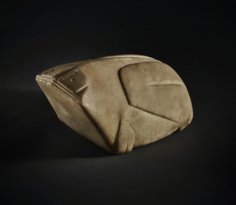 the crispness of the low-relief carving around the squarish eyes, the flat mouth-face, the big folded rear legs, and the delicately articulated spine on this melon-sized marble frog, carved like 3000 years ago in the shang dynasty, photographed by sothebys againsti a black background in 2023