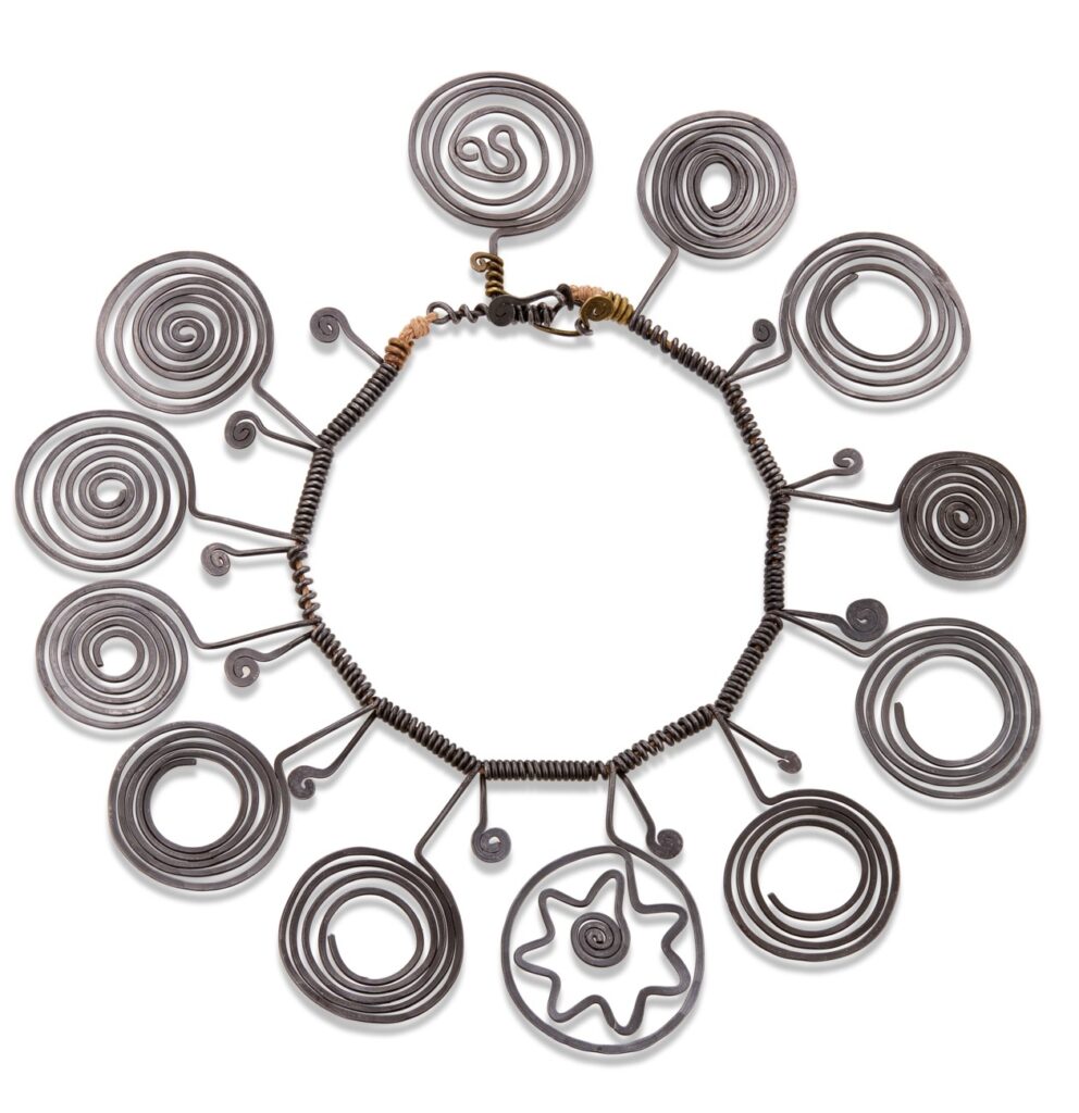 an alexander calder necklace of steel wire, in twelve segments, tightly coiled around a cord, with one end of the wire twisted into a short, stumpy spiral of one or two turns, and the longer end twisted into a medallion-sized spiral. some are tight, swirled to the center, others are open at the center, one has a squiggle, and one, at the front center, forms a flower with a central tiny spiral, surrounded by a circle. made in 1938, anne bass bought it in 1972, i guess in her hippie era. she died and now (in june 2025) it is for sale at christie's. at the moment of this typing there is one bid for $100,000.
