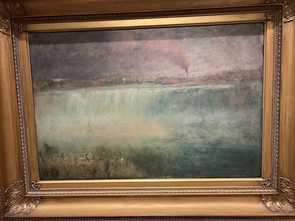a george inness painting of niagara falls is misty and indistinct in the lower, watery, bluish white half, and smoky hazy in the cloudy, smoggy purplish mauve of the smokestack spewing sky half. at the bottom left edge a thin strip of green landscape is inhabited by two tiny white flecks, presumably canvases of indistinctly painted painters. in a thick but not overly ornate gilt frame. at the smithsonian american art museum, c. 1889.