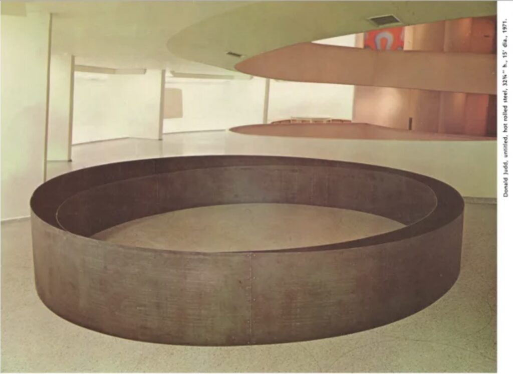 on the terrazzo ramp of the guggenheim museum sit two concentric circles of waist-high steel. the inner circle is of uniform height and thus follows the slant of the floor. the base of the outer circle is at an angle that matches the 3% grade of the ramp, leaving the top level. the discrepancy between the two is subtle but quite apparent. donald judd made this sculpture for the 1971 guggenheim international this photo was from an artforum review.