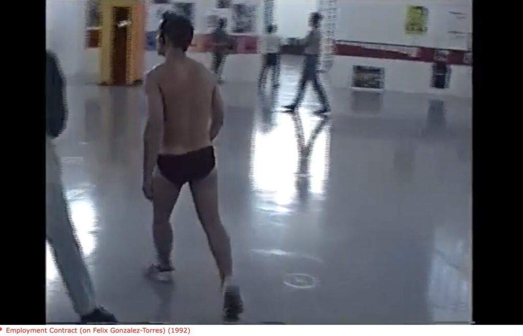 screenshot of a 1992 video of a fit young white guy in black briefs and sneakers, seen from the back as he walks through a glossy floored gallery at the kunstverein in hamburg germany, the go-go dancer for felix gonzalez-torres' work, which was on view there for the third time ever. from a video art work by the dancer, pierre bal-blanc, via ubu
