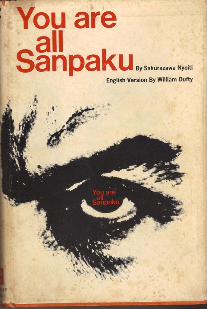 dust jacket of the 1965 edition of you are all sanpaku, written in red non-serif type above a charcoal drawing of a scowling, left eye with dark circles and more red text in the center, to make the point that sanpaku, having white below your iris, means you're evil or sick, and need brown rice