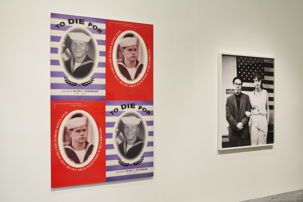 two pairs of posters by bureau are hung in a grid on a white museum wall. the two with blue and white striped background show a portrait of allen schindler, a us navy sailor murdered by the sailor depicted in the other poster, the one with a red background. schindler was murdered because he was gay. on the wall to the right is a black and white photo, large format, of a middle aged white guy and a lady in front of a clapboard building, a portrait by alix lambert and bob nickas. the installation is from a 2013 exhibition at the new museum title, nyc 1993.
