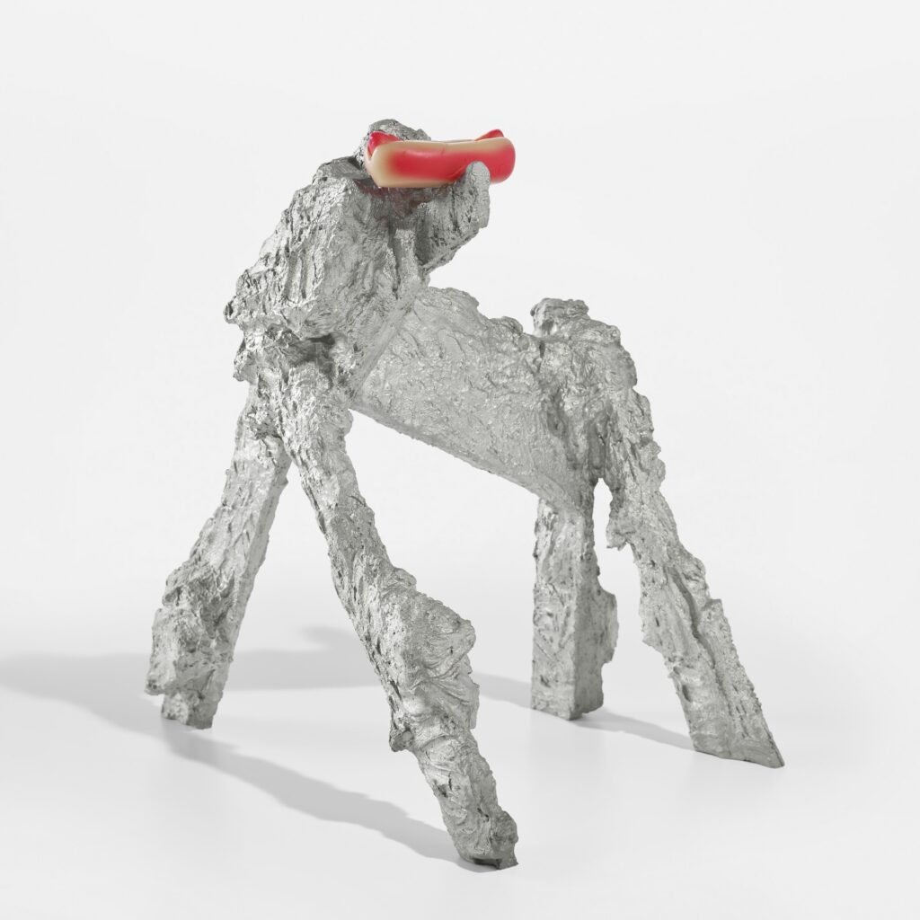 a craggy cast aluminum sculpture titled hot dog dog has the rough shape of a dog, or a wonky sawhorse barricade, with a painted urethane hot dog in a bun perched where its heasd would be. a 2011 edition by rachel harrison, this one is being flipped by kenny schachter in july 2025