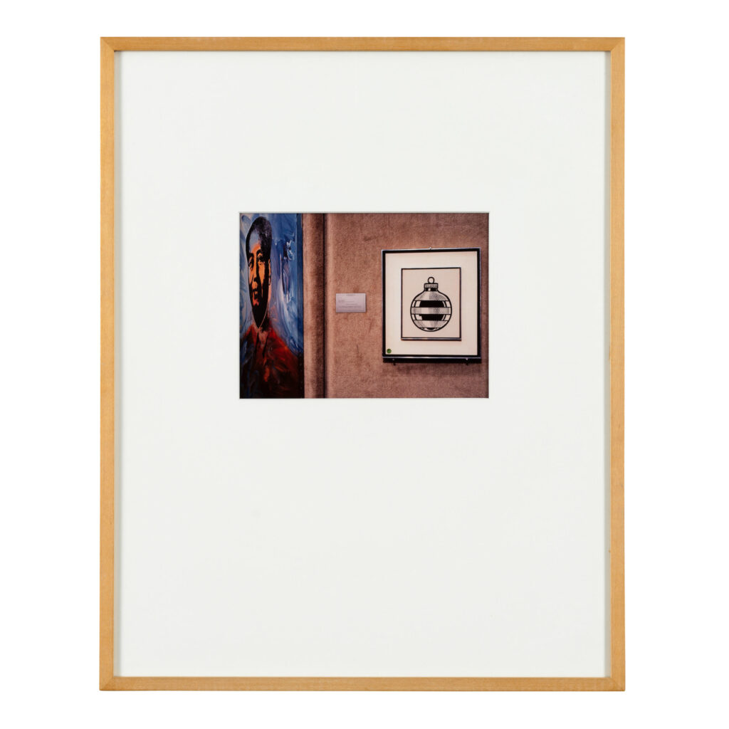 a 6 by 8 inch photo in a 20 x 16 inch frame with a giant white matte is a gift from louise lawler to roy and dorothy lichtenstein. the photo depicts a 1963 drawing in black ink by lichtstenstein of a striped glass christmas bulb, in a black frame, installed on a burlap wall at sotheby's in nyc. a blurry label is pinned next to it, and just around the corner, at an oblique angle, is part of a blue and orange warhol painting of mao. lawler titled the work warhol/lichtenstein when she gave it to them as a christmas gift, but when the edition was sold to the public it was called mao and ornament. this example is being sold at bonhams in july 2025.