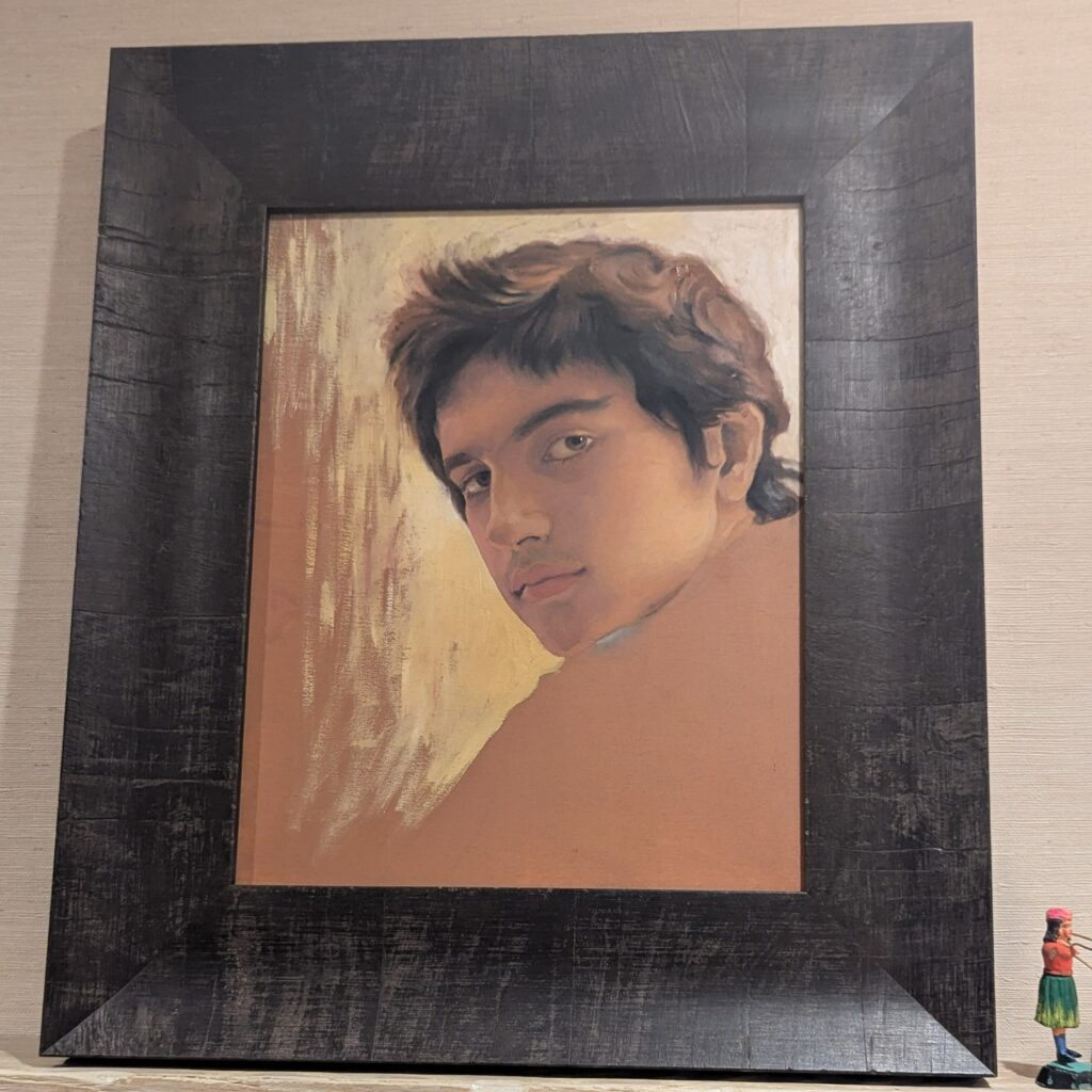 salman toor's sketchy study of a portrait of 14-yo zohran mamdani has messy dark brown and black hair, deep eyes with a serious expression, and a lot of the surrounding image left uncomplete. it is in a wide flat black wood frame on a shelf, next to a tiny painted figurine of some kind, in a photo posted on insta by amitav ghosh