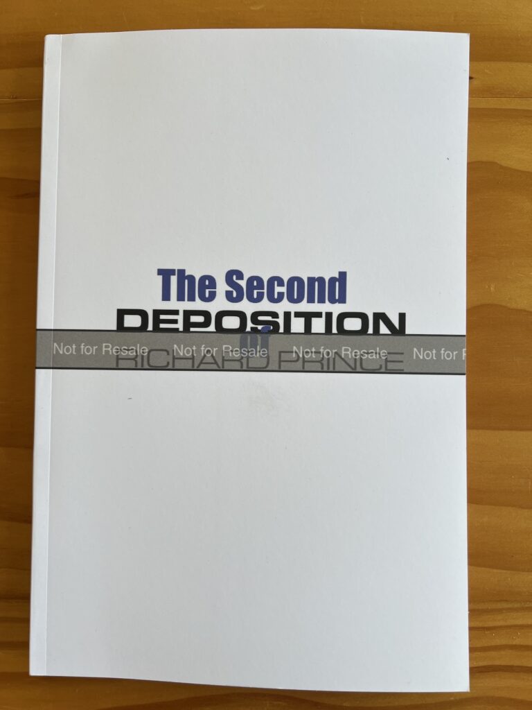 a white paperback book with the second deposition of richard prince printed on the center of the glossy cover, and a grey band wrapping across the entire cover that reads, not for resale, on a pine tabletop. the proof copy of the paperback edition, which is finna drop