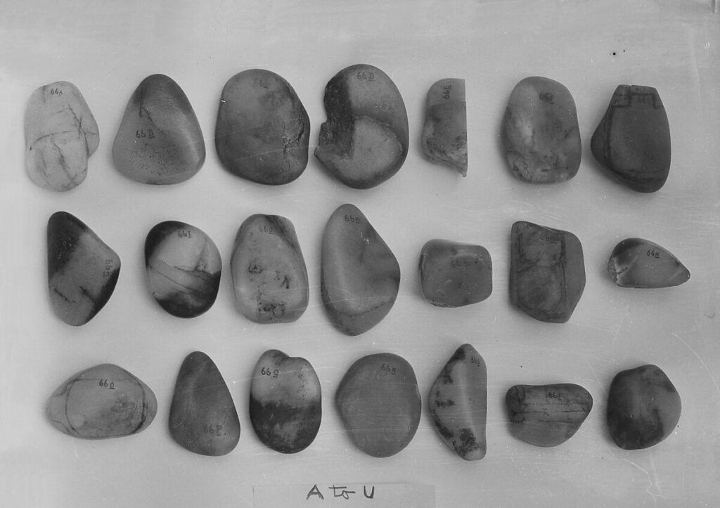 a black and white photograph of 21 small jade pebbles in three rows, with varied shades of light and dark on each, from the metropolitan museum