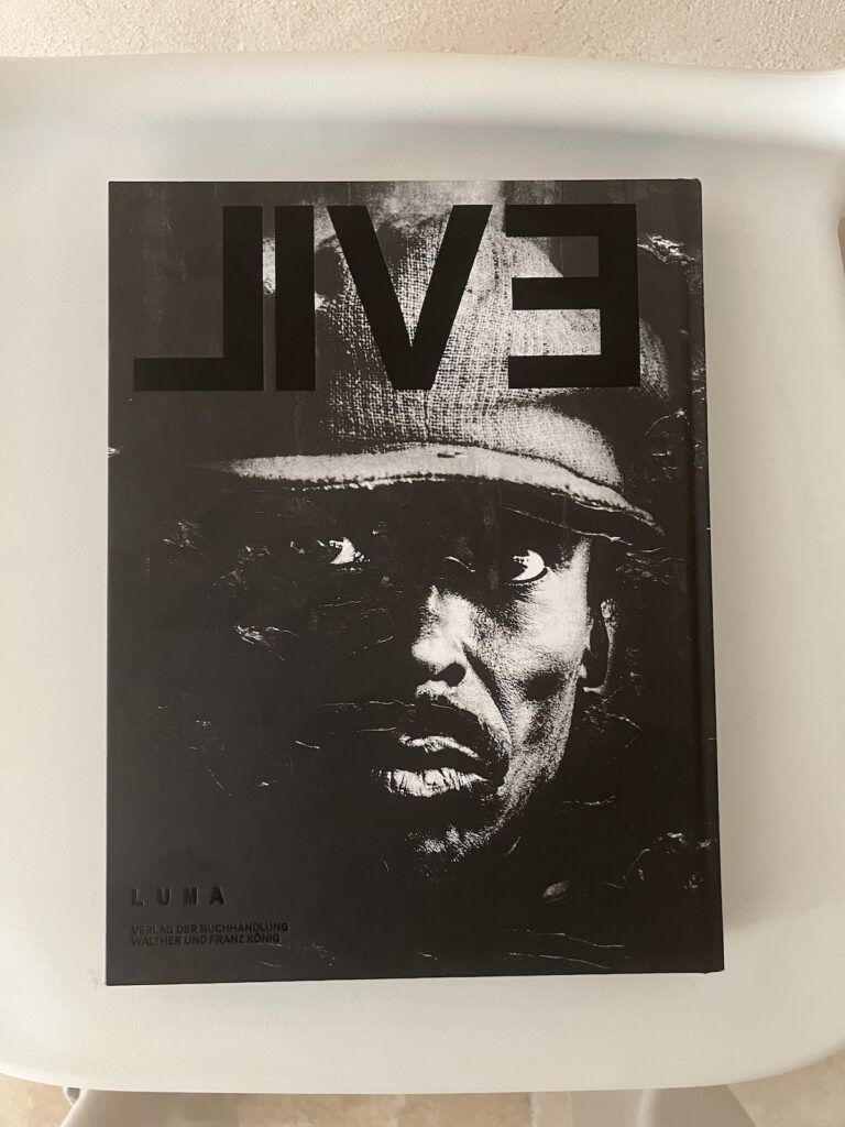 the back cover of arthur jafa's exhibition catalogue EVIL-LIVE has LIVE debossed on top of a deep black portrait of a Black man I'll identify later. the book sits on a white plastic chair